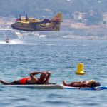 Las personas flotan en los tableros mientras un avión de Canadair vuela después de ser llenado con agua para ayudar con los esfuerzos para extinguir un gran incendio que estalló en la región de Var, en el Golfo de Saint Tropez, Francia el 17 de agosto de 2021. REUTERS / Eric Gaillard