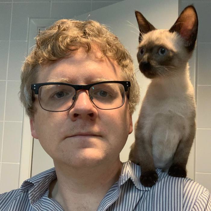 El autor con un gatito siamés posado sobre su hombro izquierdo