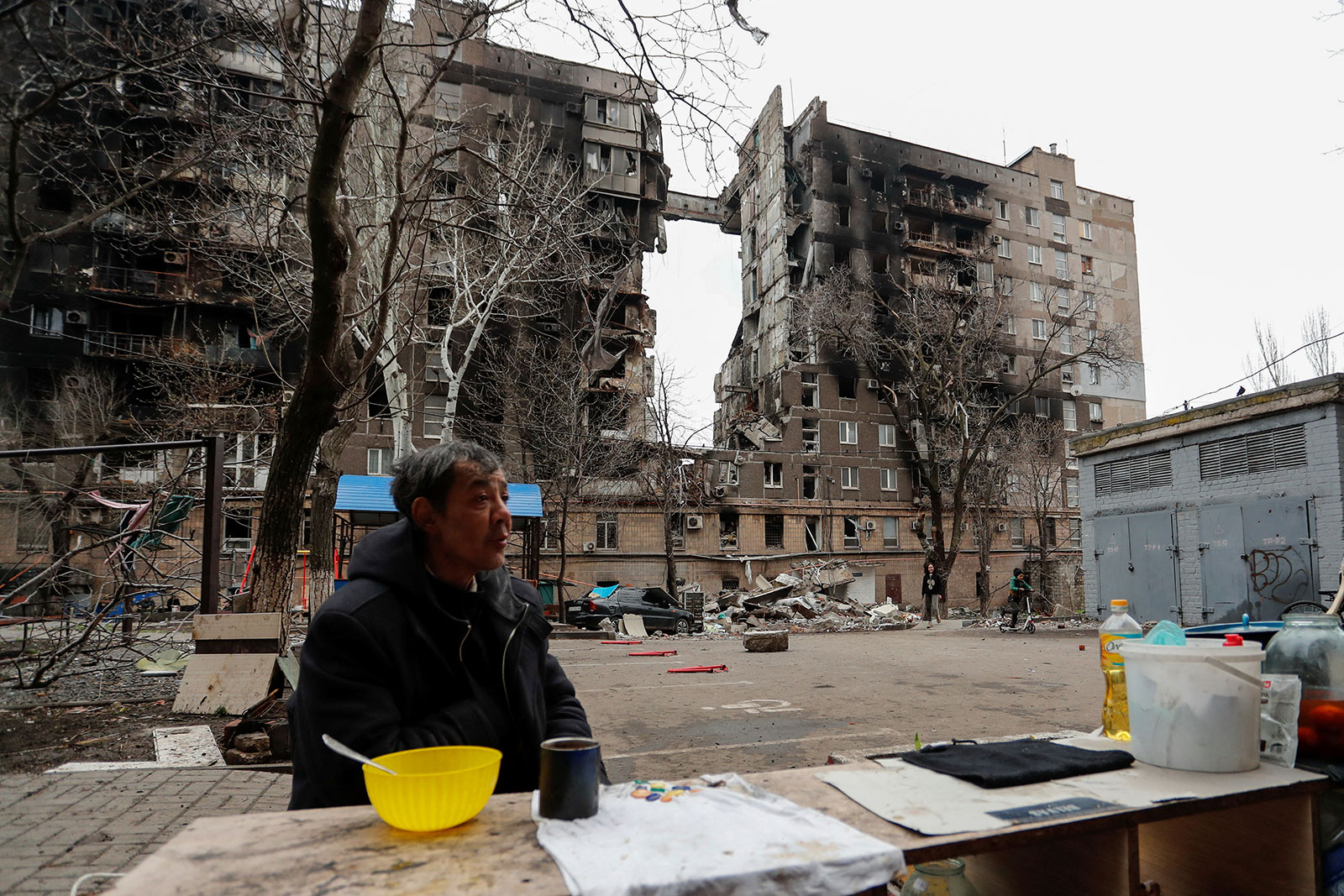 Un residente local se sienta junto a un incendio en un patio frente a un edificio dañado en Mariupol, Ucrania, el 14 de abril.