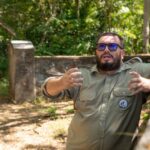 Un hombre barbudo con uniforme caqui gesticula en un patio abandonado