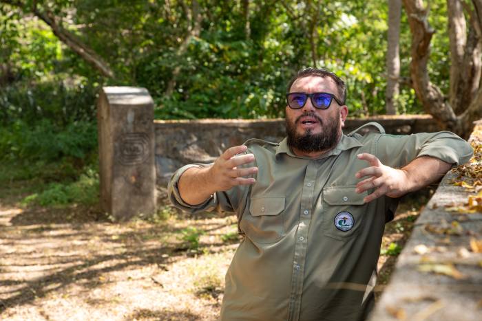 Un hombre barbudo con uniforme caqui gesticula en un patio abandonado