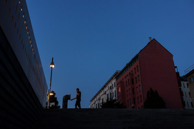 Una farola ilumina a un residente fuera de un bloque de apartamentos parcialmente iluminado al atardecer en Berlín el martes 16 de agosto.