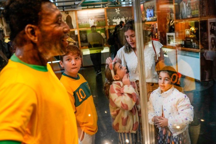 Los visitantes miran la estatua de tamaño natural de Pelé con una camiseta amarilla brillante de Brasil, con el número 10 estampado en la parte posterior, exhibida en una vitrina en el Museo Pelé en Santos, Brasil, el viernes 30 de diciembre de 2022.