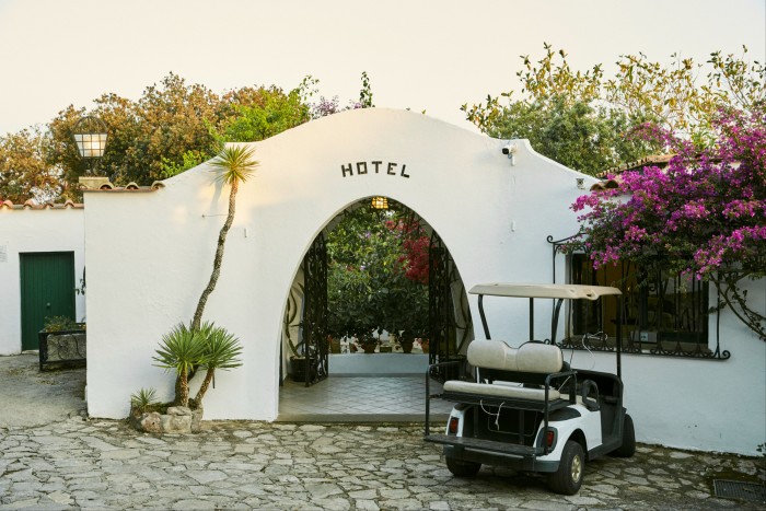La entrada del arco de estuco blanco del Hotel Punta Rossa, con un carrito de golf a la derecha y buganvillas floreciendo sobre las paredes.