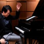 Un concertista de piano se sienta en un piano y levanta su mano izquierda dramáticamente