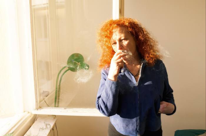 Una mujer con cabello rojo rizado sostiene un cigarrillo en sus labios.