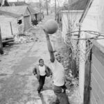 Dos niños juegan baloncesto en la calle en un barrio destartalado de una ciudad estadounidense