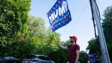 Los manifestantes sostienen banderas de la ex campaña de Donald Trump fuera del evento de campaña de DeSantis en Manchester, New Hampshire, el jueves.