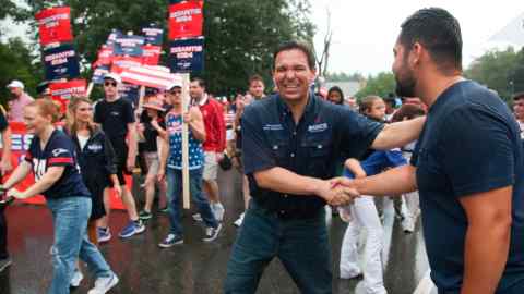 Ron DeSantis sonríe y le da la mano a un simpatizante mientras está rodeado de otros simpatizantes que sostienen carteles de 'DeSantis 2024'