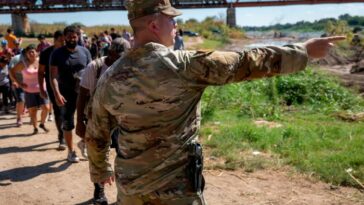 Un soldado de la Guardia Nacional de Texas señala a los migrantes hacia un puesto de control de la Patrulla Fronteriza de EE. UU.