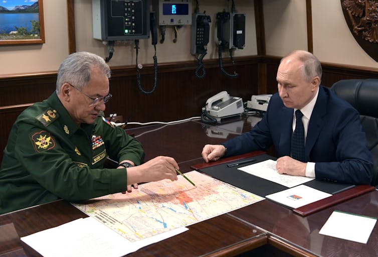 El ministro de Defensa ruso, Sergei Shoigu, sentado frente a Vladimir Putin, señala un mapa.