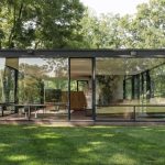 Una casa de cristal modernista situada en un paisaje verde y exuberante. La estructura tiene grandes ventanales de piso a techo en todos los lados.