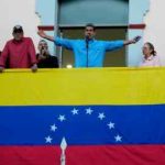 Un hombre extiende los brazos en un balcón cubierto con la bandera de Venezuela.