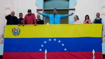 Un hombre extiende los brazos en un balcón cubierto con la bandera de Venezuela.