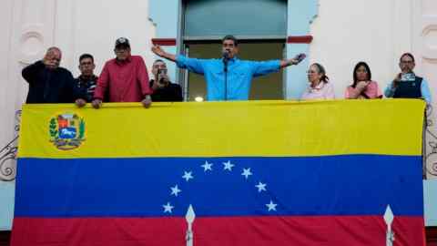 Un hombre extiende los brazos en un balcón cubierto con la bandera de Venezuela.