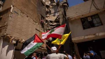 Un hombre sostiene banderas palestinas, libanesas y de Hezbolá junto a un lugar dañado donde fue asesinado el principal comandante de Hezbolá, Fuad Shukr.