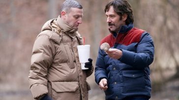 Dos hombres, al aire libre, con abrigos, uno de los cuales le ofrece al otro un hongo.