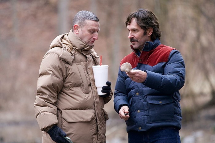 Dos hombres, al aire libre, con abrigos, uno de los cuales le ofrece al otro un hongo.