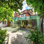 Una elegante ampliación en la planta baja y el patio trasero de una casa adosada del siglo XIX en Londres. La ampliación está hecha de vidrio con marcos de metal, mientras que el resto del edificio está hecho de ladrillo.