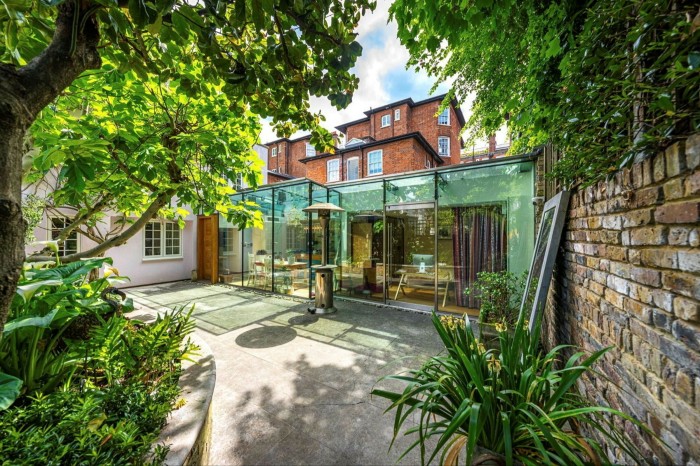 Una elegante ampliación en la planta baja y el patio trasero de una casa adosada del siglo XIX en Londres. La ampliación está hecha de vidrio con marcos de metal, mientras que el resto del edificio está hecho de ladrillo.