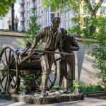 Una estatua de bronce de un hombre tirando de un carro cargado de pertenencias. Un niño se sienta en lo alto y una mujer camina a su lado.