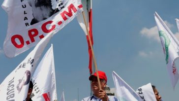 Los manifestantes en la Ciudad de México sostienen banderas y pancartas mientras se manifiestan contra la reforma judicial. Un hombre con gorra roja y camisa a cuadros sostiene de manera prominente una bandera, mientras otros se reúnen a su alrededor.