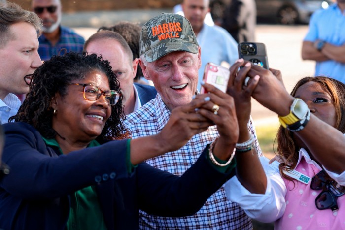 Bill Clinton, con una gorra con 'Harris Walz', se hace selfies con sus entusiastas seguidores sosteniendo teléfonos.