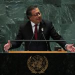 Un hombre vestido con traje oscuro, camisa blanca y corbata roja habla en un podio con el emblema de las Naciones Unidas frente a él, indicando que se dirige a una audiencia.