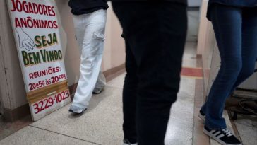 La gente camina junto a un cartel de una sesión grupal de Jugadores Anónimos en Sao Paulo, Brasil.