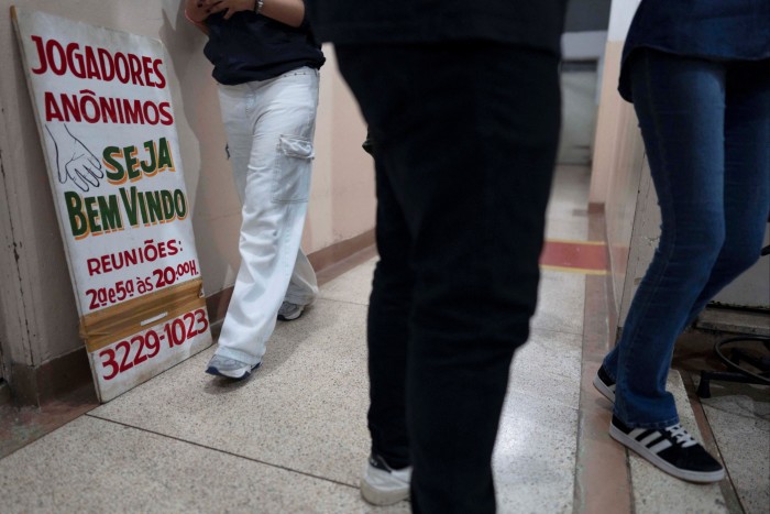 La gente camina junto a un cartel de una sesión grupal de Jugadores Anónimos en Sao Paulo, Brasil.