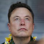 Elon Musk, con un collar de flores amarillas, mira hacia arriba