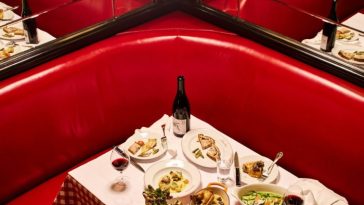 Un banco esquinero de cuero rojo junto a paredes de espejos en Le Veau d'Or, alrededor de una mesa llena de platos franceses clásicos