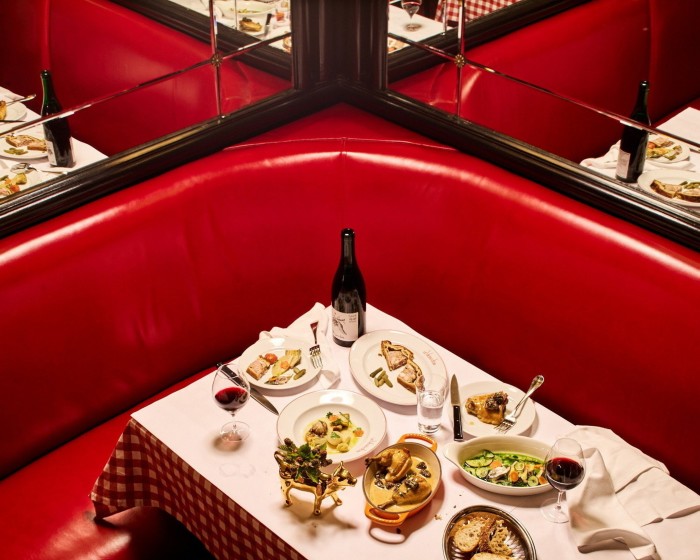 Un banco esquinero de cuero rojo junto a paredes de espejos en Le Veau d'Or, alrededor de una mesa llena de platos franceses clásicos