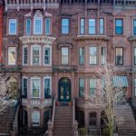 Una hilera de casas adosadas de piedra rojiza con escalones hasta las puertas de entrada. La casa del medio está a la venta por 1,5 millones de dólares.