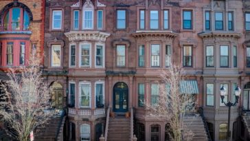 Una hilera de casas adosadas de piedra rojiza con escalones hasta las puertas de entrada. La casa del medio está a la venta por 1,5 millones de dólares.