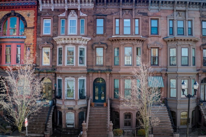 Una hilera de casas adosadas de piedra rojiza con escalones hasta las puertas de entrada. La casa del medio está a la venta por 1,5 millones de dólares.