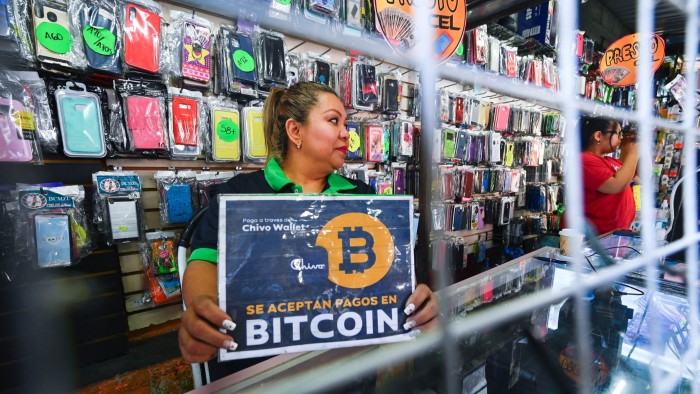 A vendor holds a sign reading ‘Bitcoin accepted’ at a store in San Salvador