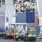 Un contenedor de envío colocado en un camión junto a un barco atracado en un puerto de EE. UU.