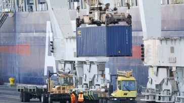 Un contenedor de envío colocado en un camión junto a un barco atracado en un puerto de EE. UU.