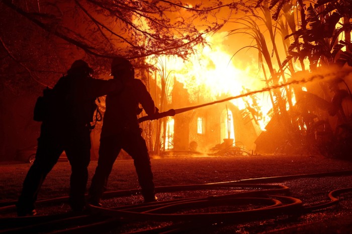 Los bomberos rocían agua sobre una casa en llamas mientras el incendio Eaton avanzaba por el área en Altadena, California, el miércoles.