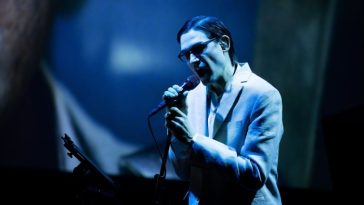 Una cantante con gafas oscuras canta apasionadamente frente a un micrófono.