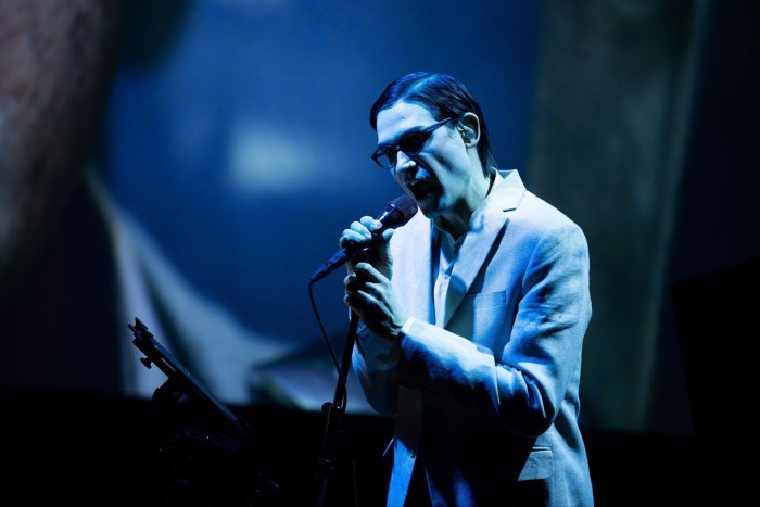 Una cantante con gafas oscuras canta apasionadamente frente a un micrófono.