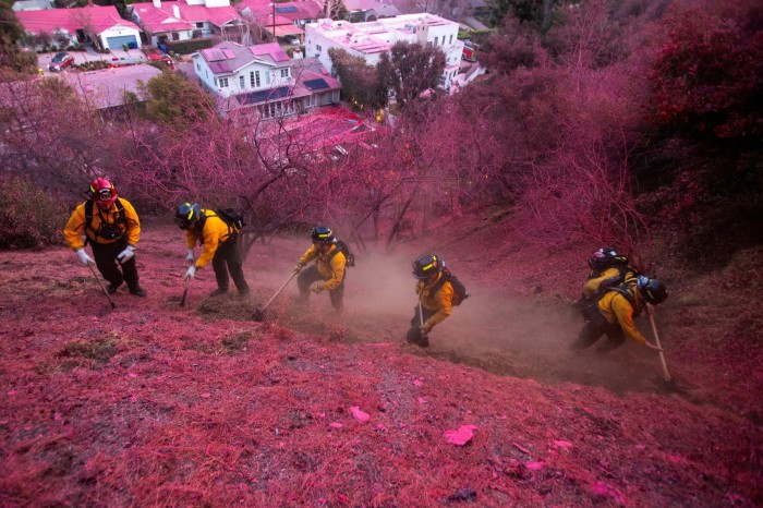 Los bomberos trabajan para despejar un cortafuegos en una ladera cubierta con retardante en Palisades Fire