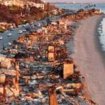 Una vista aérea de vehículos de reparación al atardecer pasando cerca de casas frente a la playa que se quemaron en el incendio de Palisades.