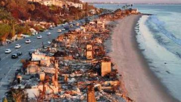 Una vista aérea de vehículos de reparación al atardecer pasando cerca de casas frente a la playa que se quemaron en el incendio de Palisades.