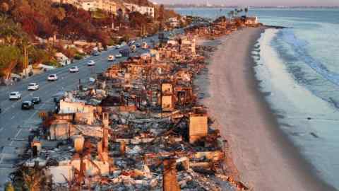 Una vista aérea de vehículos de reparación al atardecer pasando cerca de casas frente a la playa que se quemaron en el incendio de Palisades.