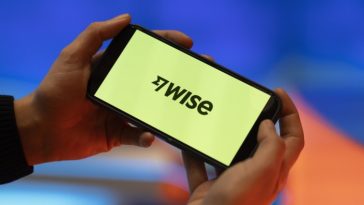 Hands holding a smartphone displaying the Wise Plc logo on the screen.