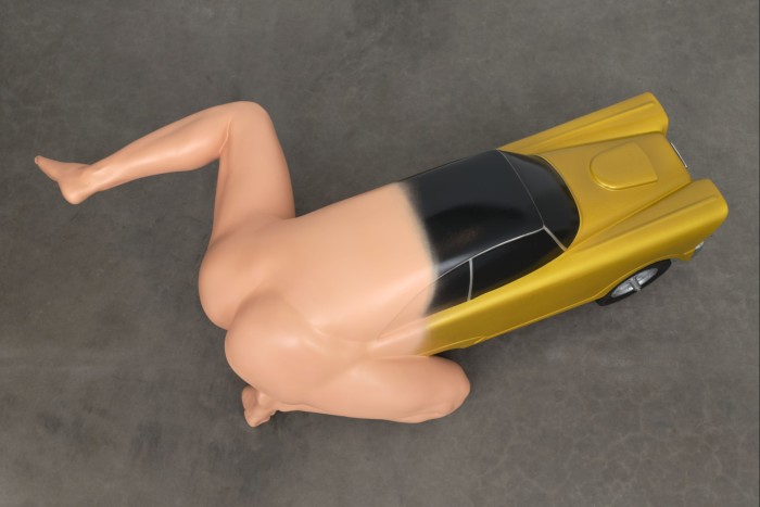 Escultura que representa la mitad inferior desnuda de un hombre transformándose en un auto dorado