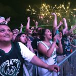 Un grupo de fanáticos entusiasmados detrás de una barrera celebrando mientras los fuegos artificiales iluminan el cielo nocturno