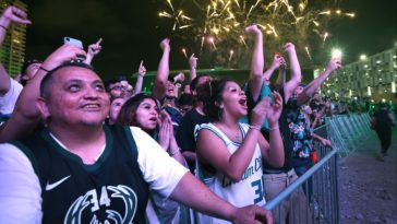 Un grupo de fanáticos entusiasmados detrás de una barrera celebrando mientras los fuegos artificiales iluminan el cielo nocturno